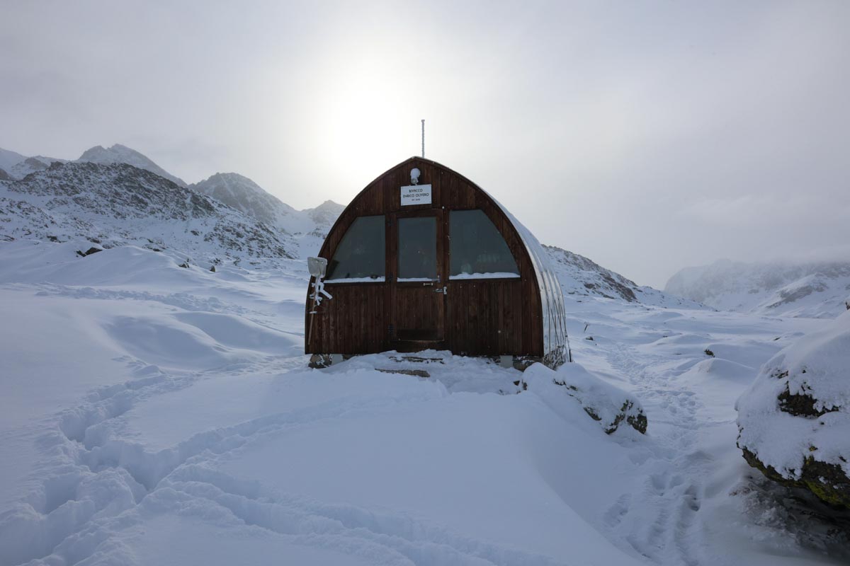 Bivouac Olivero, cabane d'architecte à l'enveloppe extérieur en métal réfléchissant, dans un décor de montagnes enneigées Bivouac Olivero, cabane d'architecte à l'enveloppe extérieur en métal réfléchissant, dans un décor de montagnes enneigées