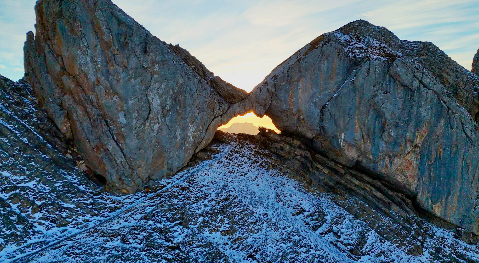 Trou de la mouche, arche en pierre dans les aravis baignée d'une lueur matinale, avec en arrière plan la tournette