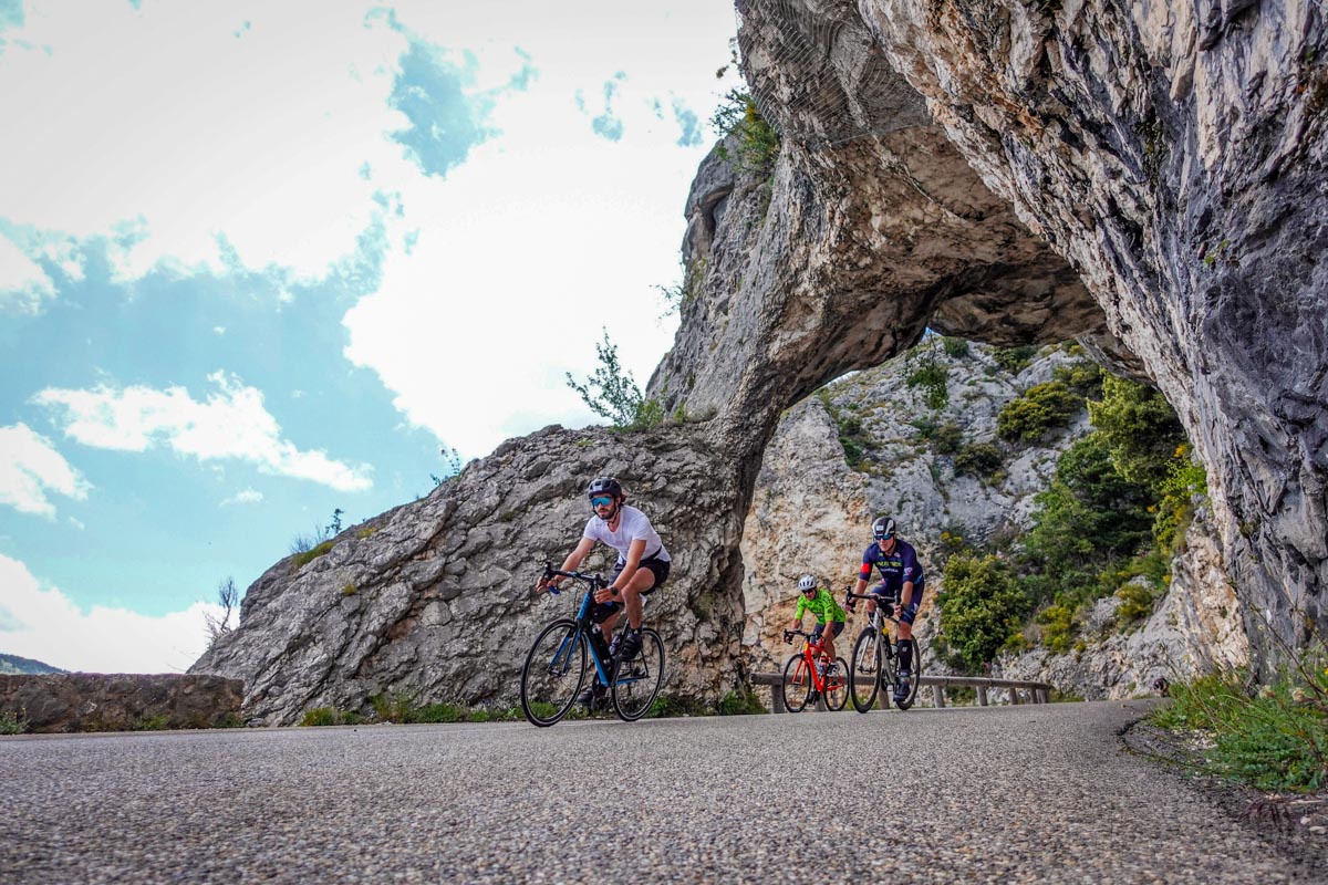 Cycliste cheveux au vent dans une descente rapide sous un arche en calcaire blanc dans les gorges du Loup