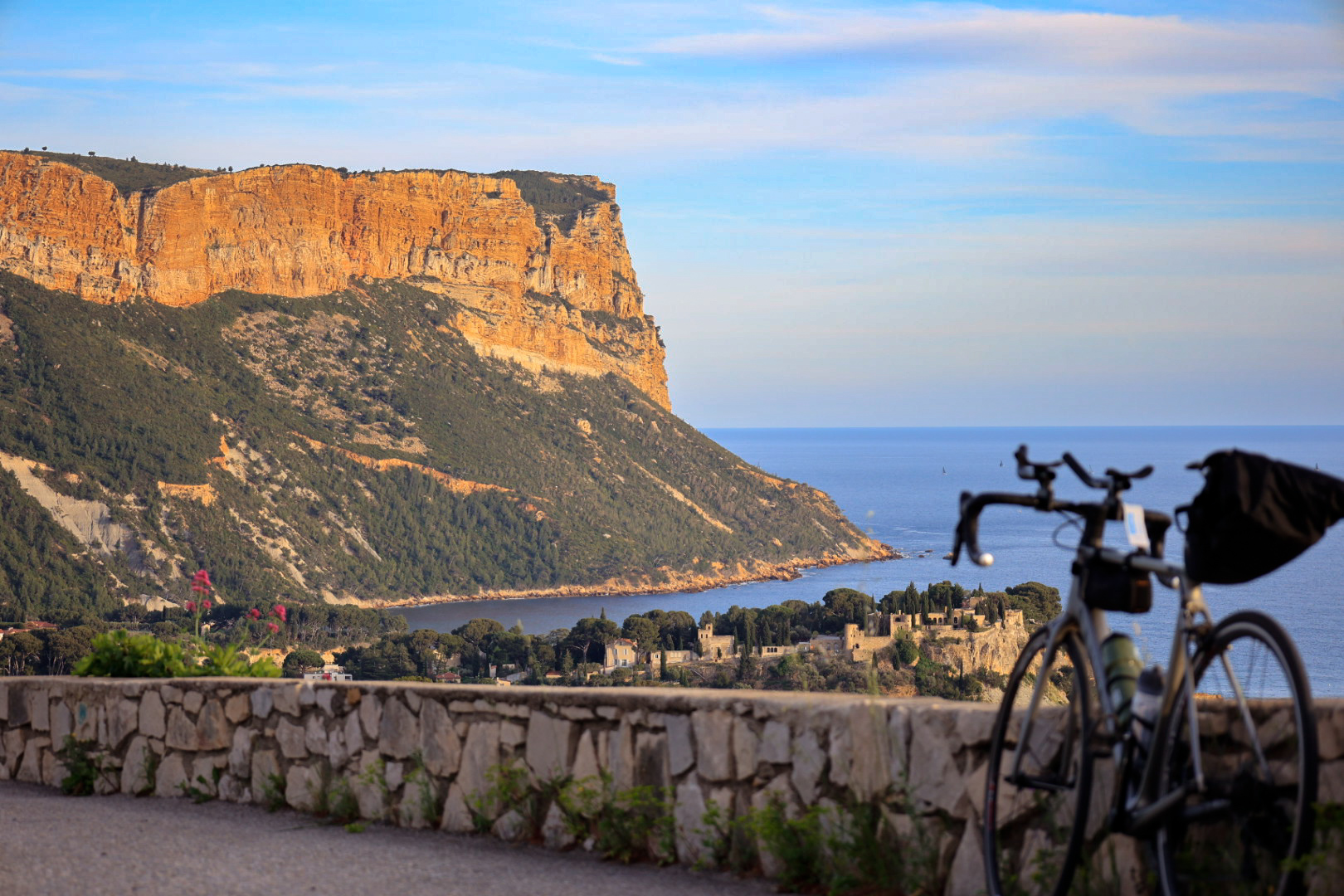 Cap canaille plogeant dans la mer avec et sa roche rouge avec au premier plan un vélo de route flamboyant sur la route de la Gineste