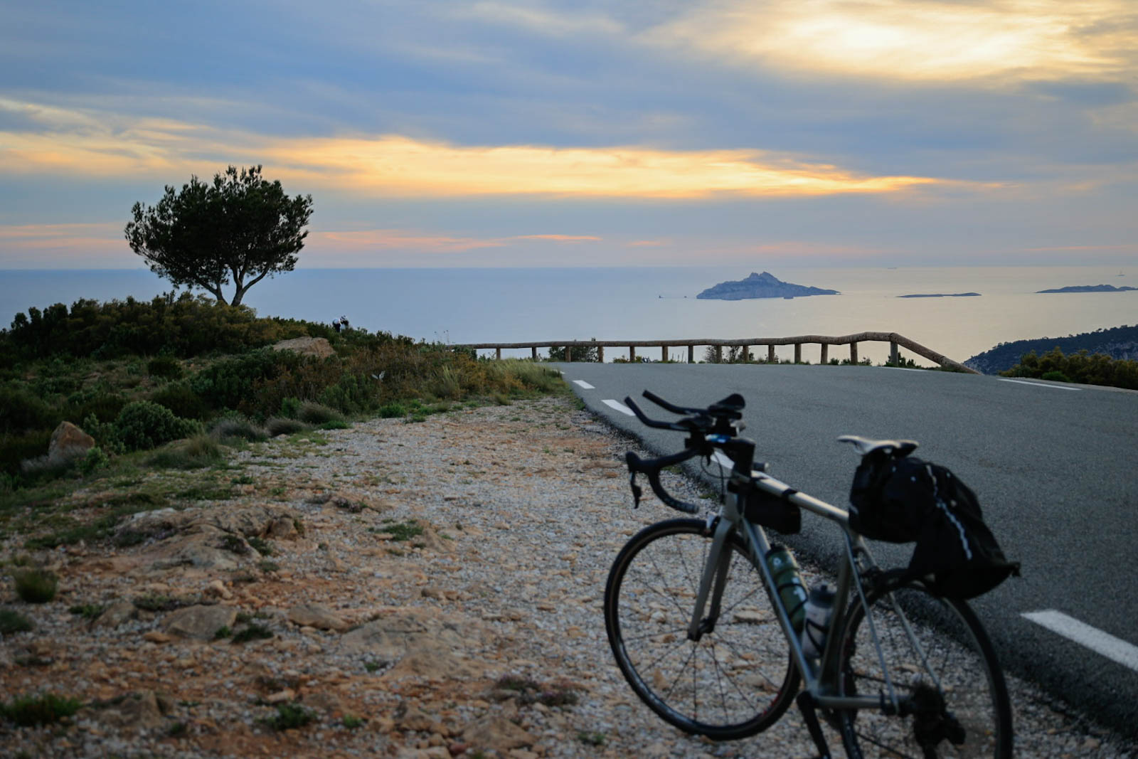 photo d'un vélo sur la route des crêtes avec en arrière plan les calanques de cassis dans la lumière orangé sd'un soleil couchant 